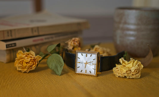 A vintage watch rests amid flowers and books.